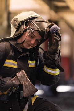 female firefighter portrait wearing full equipment and emergency rescue equipment. taking off oxygen mask after successful intervention. smoke and fire trucks in the background.