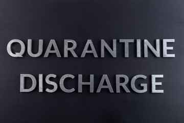 the words quarantine discharge laid with silver metal letters on matte back flat surface directly...