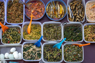 Overhead shot of people buying food over variety of delicious Malaysian home cooked dishes sold at street market stall in Kota Kinabalu, island Borneo, Malaysia