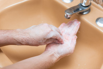 Woman lathering hands with soap in a yellow sink at home to prevent COVID-19 spread