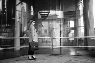 Young attractive caucasian businesswoman with mask and bag in front of company