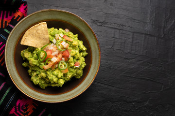 Mexican guacamole with tomato and serrano pepper on dark background