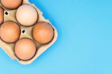 Raw brown chicken eggs on blue background .