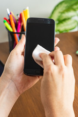 Woman's hand cleaning a smartphone with a white tissue in a home office ambient