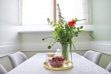 Bouquet of flowers in vase, tray with ripe strawberries