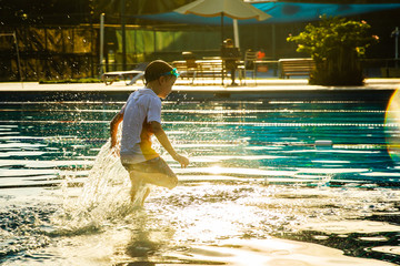 Happy little kid running into water in the swimming pool during his initial swimming lessons