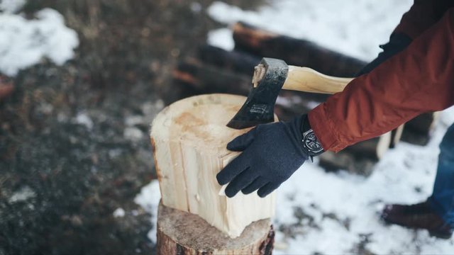 Men's hands in gray gloves and watches holding an axe and chopping wood in winter. Close up