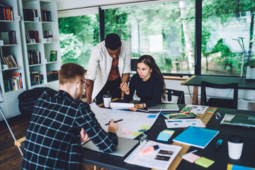Smart casual engineers collaborating on blueprint sketch brainstorming on productive analyzing, multicultural male and female colleagues briefing during education learning in coworking space