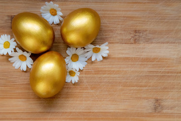 Ester golden eggs and daisies on wooden rustic table.