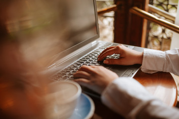 Close up of  a young girl typing on a keyboard lap top next to a cup of coffee
