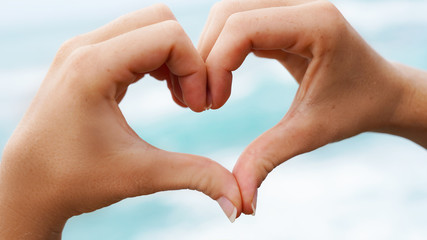 love sign on blue ocean water background. female hands show a symbol