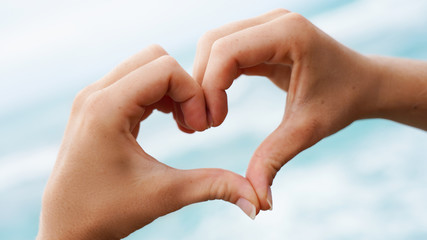 love sign on blue ocean water background. female hands show a symbol