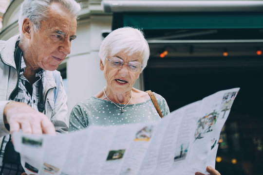 Senior woman reading map while standing with partner in city during vacation