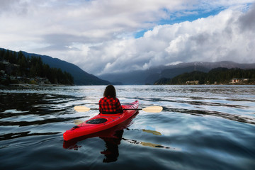 Adventurous Girl Paddling on a Bright Red Kayak in calm ocean water during a vibrant and colorful...