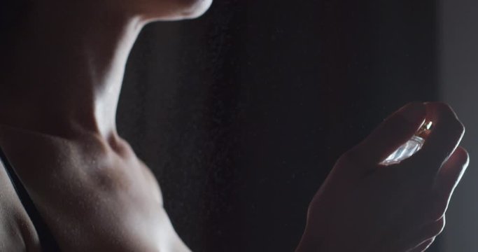 Close up shot of an young woman is spraying a fragrance with scent particles on her wet skin after taking a shower in an evening. Concept of femininity, sensuality,perfume, skin care, cosmetics
