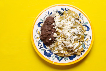 Mexican green chilaquiles with beans on yellow background