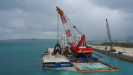 Floating crane platform with a huge bucket extracts sand from the bottom of the Pacific Ocean.
a huge crane extracts white sand from the ocean off the coast of Okinawa.