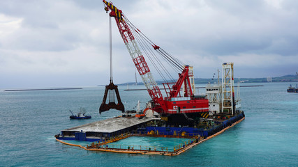 Fototapeta premium floating crane platform with a huge bucket extracts sand from the bottom of the Pacific Ocean. a huge crane extracts white sand from the ocean off the coast of Okinawa.