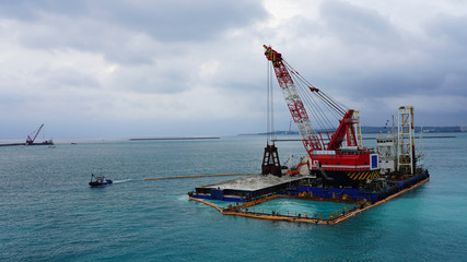 floating crane platform with a huge bucket extracts sand from the bottom of the Pacific Ocean.
a huge crane extracts white sand from the ocean off the coast of Okinawa.