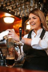 A young attractive blonde caucasian  waitress pouring beer in a cafe