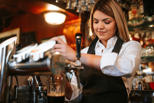 A young attractive blonde caucasian  waitress pouring beer in a cafe - Powered by Adobe