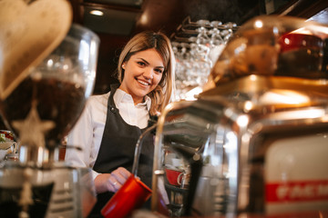 A young attractive caucasian blonde waitress makes coffee in a cafe