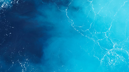 Bright color of sea foaming water. The texture of the water. Natural background, dark and light blue. Aerial drone shot