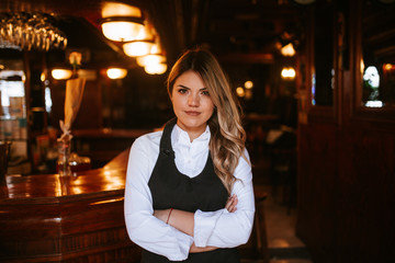 Portrait of young attractive caucasian blonde waitress at cafe entrance