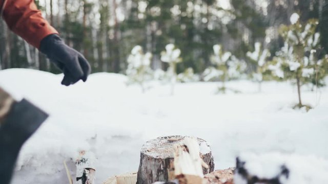 Men's hands in gray gloves hold an axe and chop wood in winter. Close up.