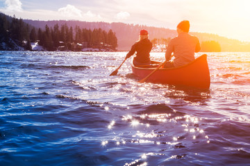 Couple friends on a wooden canoe are paddling in water during a vibrant sunny day. Taken in Indian Arm, near Deep Cove, North Vancouver, British Columbia, Canada. Concept: Adventure, Sport, Explore