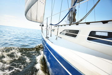 White yacht sailing on a sunny summer day. Close-up view from the deck to the bow and sails. Waves...