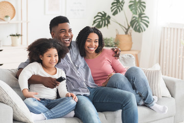 Black family of three relaxing on couch, watching tv together