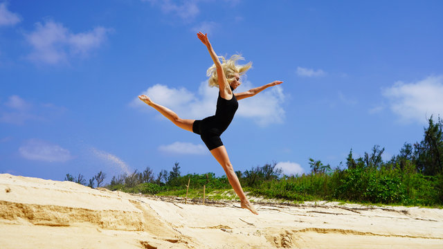 beautiful blonde girl dancer jumping on the white sand. gymnast doing the splits in the air against a blue sky. freedom to jump in sunny weather. gymnastic split  