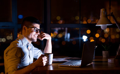 Guy Sitting At Laptop Having Coffee In Office At Night