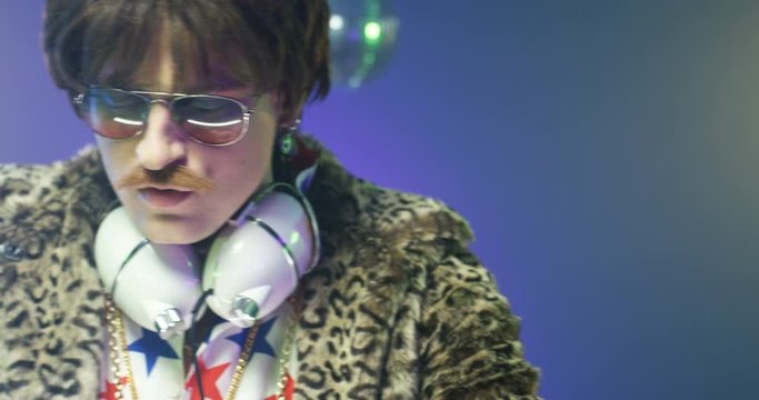 Close up Caucasian stylish vintage male dj mixing music on sound equipment at party. Retro style funny man with sunglasses and headphones dancing while playing disco in leopard jacket. Club concept
