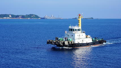 Colored tugboat works in port. bright tugboat in blue water. industrial ship on waves tropical...
