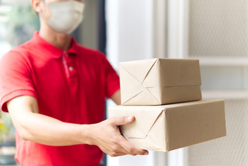 Asian postman, deliveryman wearing mask carry small box deliver to customer in front of door at home. Man wearing mask prevent covid19, corana virus affection outbreak. Social distancing work concept.