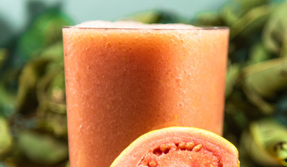 Glass of guava juice (Psidium guajava L.) between leaves and fruits on a neutral background