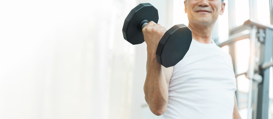 Happy Asian Senior Fitness man lifting dumbbell while exercise at the gym. Strong Sporty Elderly...
