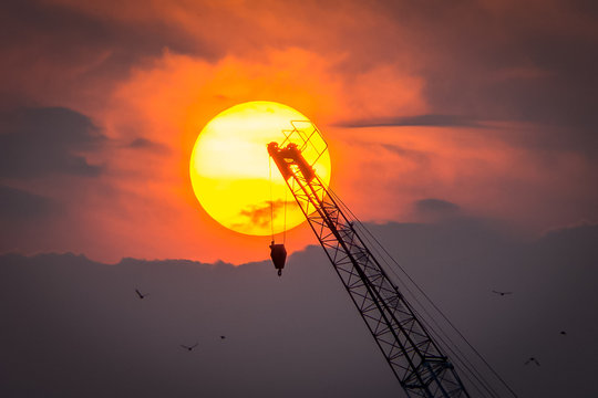 Low Angle View Of Silhouette Crane Against Sun In Cloudy Sky At Sunset