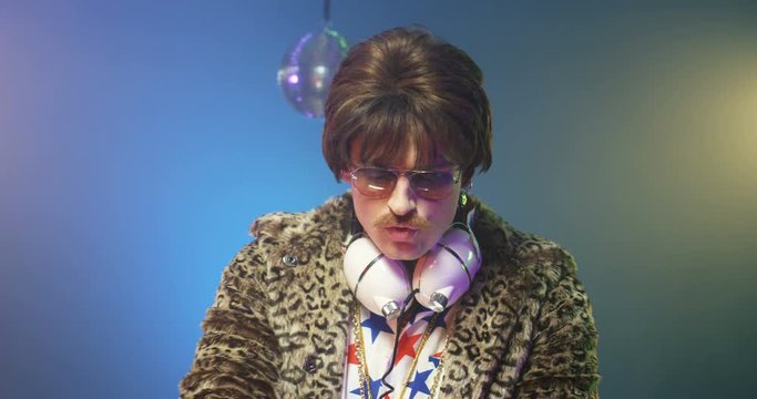 Caucasian retro style man in leopard jacket mixing music on sound equipment at party. Stylish vintage male DJ with sunglasses and headphones dancing while playing disco. Clubbing lifestyle 50s concept