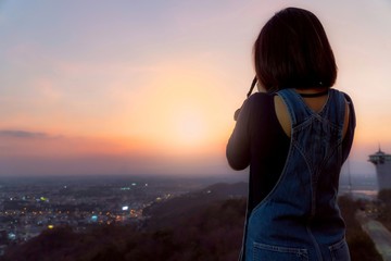 Fototapeta premium shot-haired asian women, wearing a denim bib, were standing tall and using a camera to photo in a city with bright lights in the evening in dusk sky