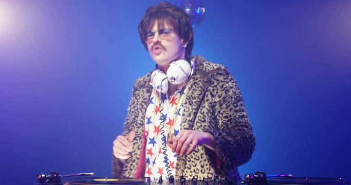 Stylish male dj touching vinyl while playing music at party. Retro style funny Caucasian man with headphones in leopard jacket mixing sounds on stereo equipment at nightclub. Vintage concept