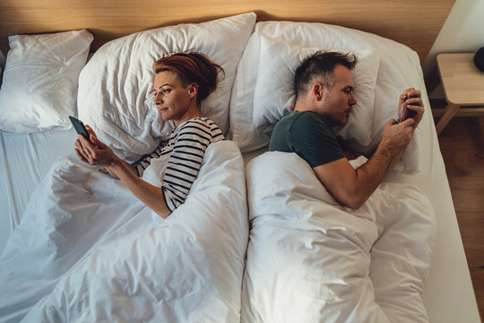 Couple laying in the bed with their backs turned and using smartphone
