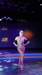 beautiful brunette posing in front of the camera on stage. girl ballroom dancer in the spotlight, sexy sensual girl in a dance leotard and necklace on a dark blue background