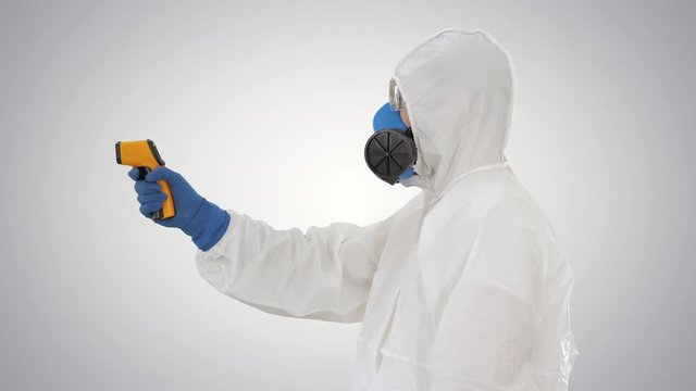 Temperature check on a corona virus Doctor in protective suit with pyrometer on gradient background.