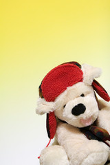 A stuffed dog wearing a red hat in front of a gradated yellow background.