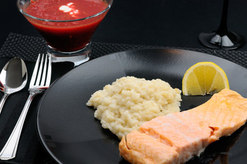 Black table setting with plate of salmon and risotto with borscht soup