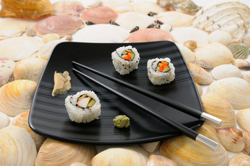 Crab Uramaki sushi and chopsticks on a black plate surrounded by sea shells