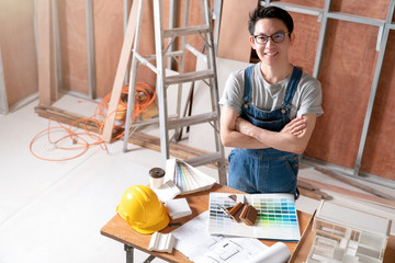 asian attractive glasses interior designer working at house site renovation construction progress with smile and confident at desk with blue print and drawing tool